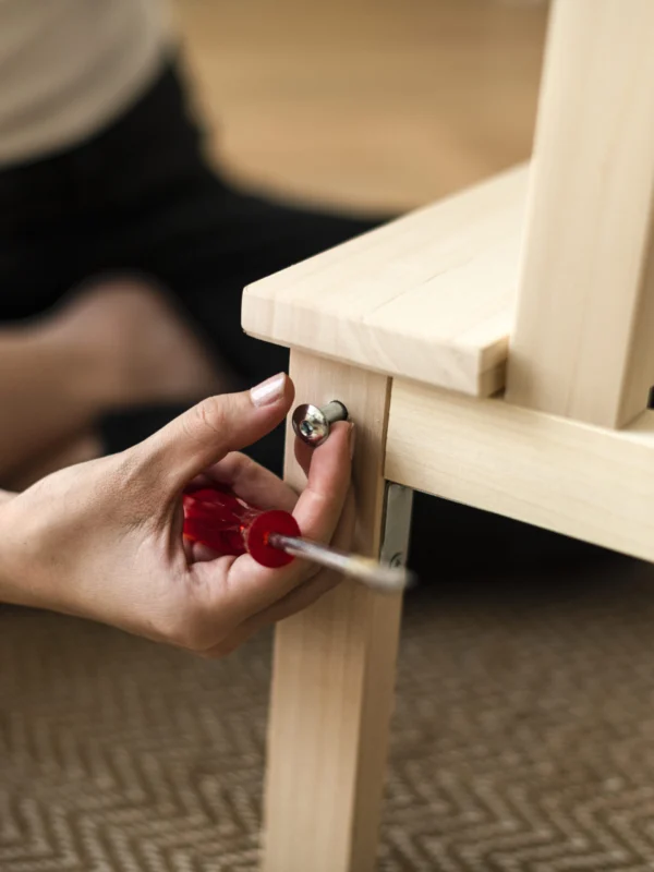 Manos montando la pata de una mesa de madera con un destornillador