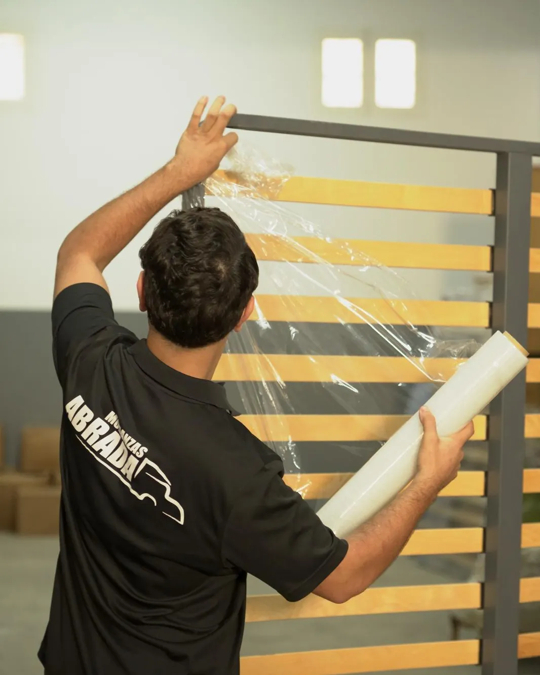 Operario de Mudanzas Abrada envolviendo con film transparente un cabecero de listones de madera en el almacén