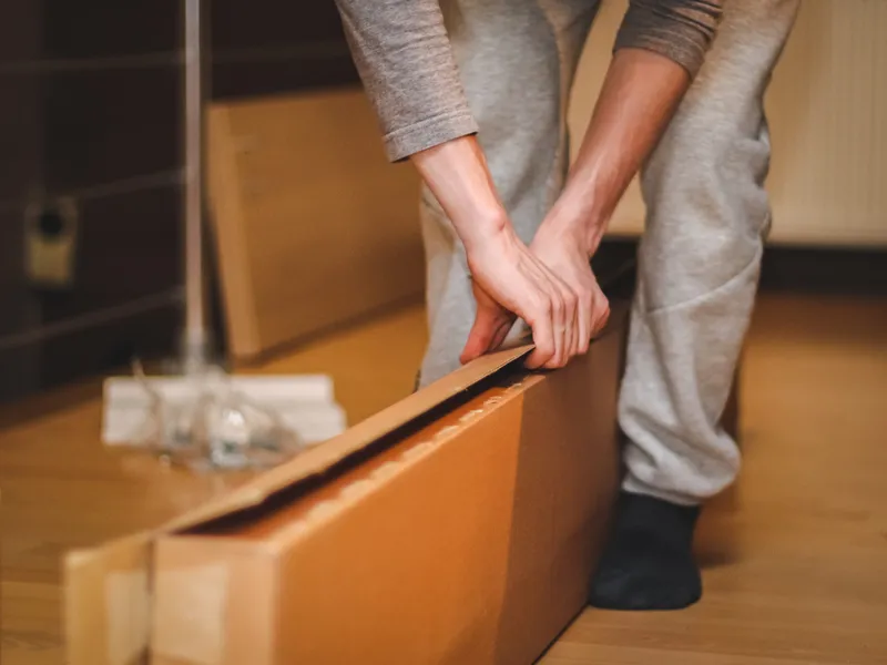 Manos cerrando una caja de carton apoyada en el suelo de madera de una vivienda